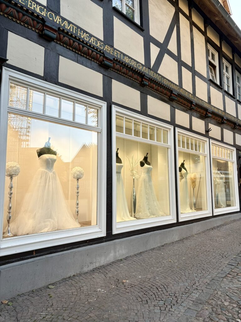 In einem Schaufenster eines Brautmodengeschäfts in einer Kopfsteinpflasterstraße sind Brautkleider auf Schaufensterpuppen ausgestellt.