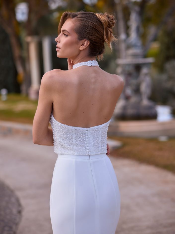 Eine Frau in einem weißen, trägerlosen, mit Perlen bestickten Brautkleid steht im Freien, mit dem Rücken zur Kamera, und trägt ihr Haar hochgesteckt – eine elegante Braut, bereit für ihren großen Tag.