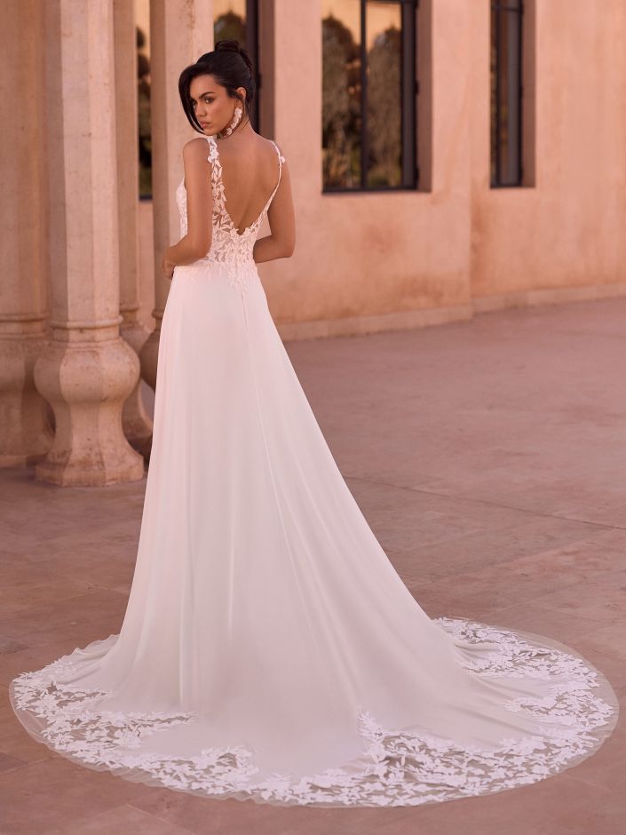 Eine Frau in einem eleganten weißen Brautkleid mit Spitzendetails, die im Freien steht und mit dem Rücken zur Kamera.